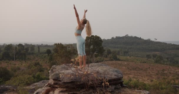 Mujer de pie sobre roca cambiando posiciones de yoga y un hermoso paisaje con árboles — Vídeos de Stock