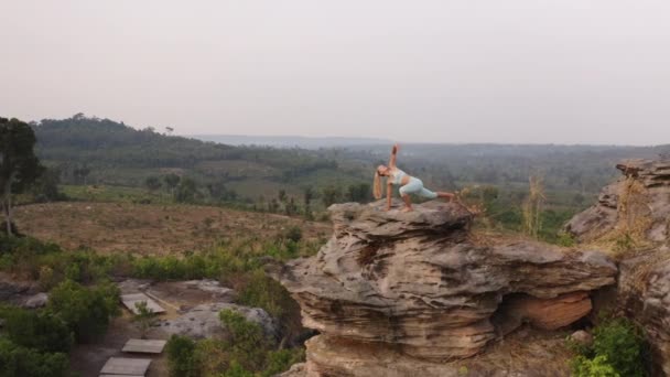 Drone shot van een vrouw door de grote rots in de bergen doet yoga oefeningen — Stockvideo