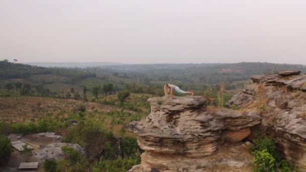 Aerial panorering Skott av kvinnliga gör revolterade triangeln Yoga Pose av klipporna i bergen — Stockvideo