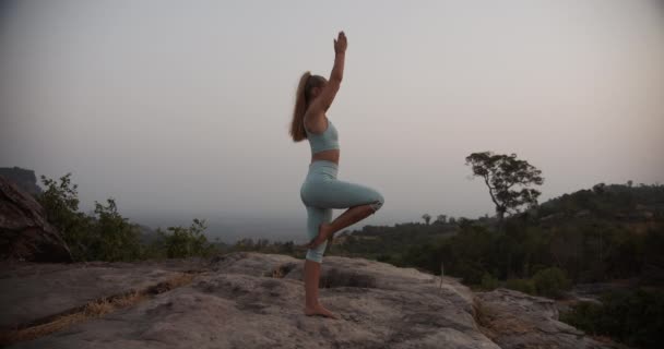 Female with Blonde Hair Shifting from One Yoga Pose to Another on Top of the Mountains — Stock Video