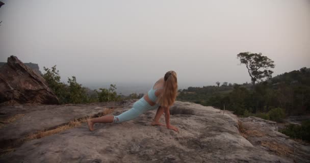 Kobieta robi zbuntowany trójkąt jogi Pose w spokojnym górskim krajobrazie — Wideo stockowe