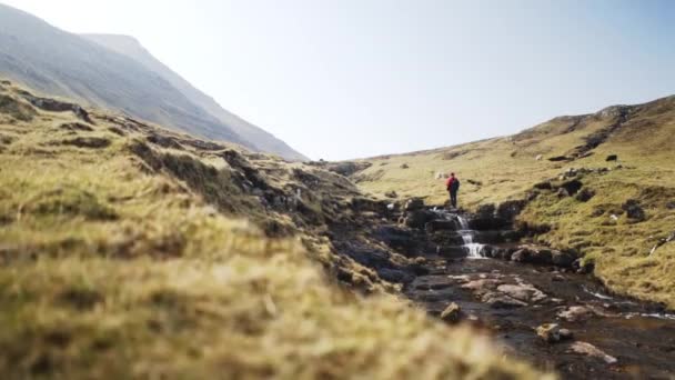 Панорамный кадр воды из ручья и человека, стоящего в скале на Фарерском острове — стоковое видео