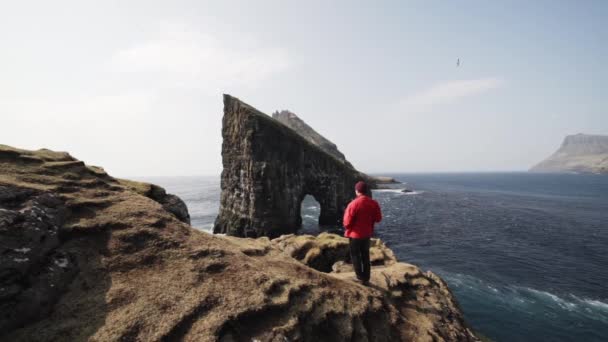 Man Standing in Rocky Cliffs Overviewing Large Rock in Faerské ostrovy — Stock video