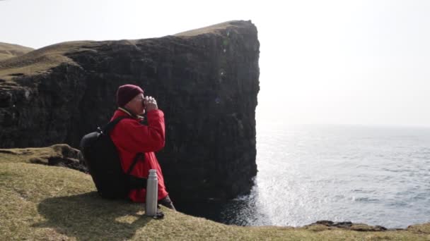 Muž Pití z poháru termální láhve s výhledem na Drangarnir Rock v Faerských ostrovech — Stock video
