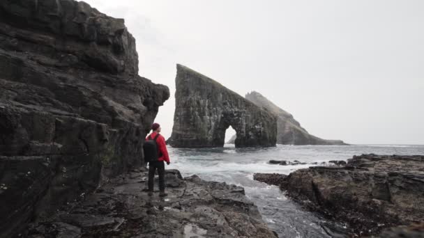 Drangarnir båge och en manlig resenär står vid klipporna beundrar utsikten — Stockvideo