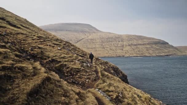 Homme marchant au pied de la colline entourée d'eaux de mer bleu profond calme — Video