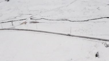 Etrafı karla kaplı yol kenarı ve yoldan geçen bir araba.