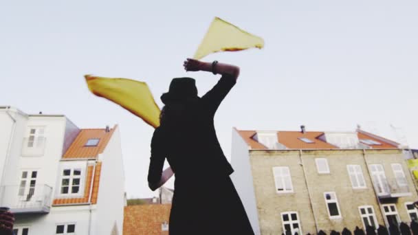 Rücken einer Frau vor der Kamera, während sie zwei gelbfarbene Fahnen schwenkt — Stockvideo