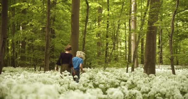 Geschwister beobachten aufmerksam ihren Schritt, während sie von weißen Blumen umgeben sind — Stockvideo