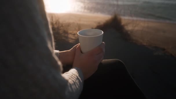 Mulher segurando xícara de café na praia iluminada pelo sol — Vídeo de Stock
