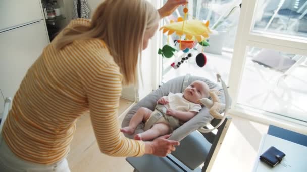 Mãe segurando brinquedos sensoriais e coloridos bebê bonito sobrecarga na cadeira de balancim — Vídeo de Stock