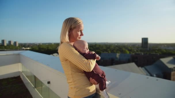 Mamá sosteniendo a su bebé de forma segura en brazos mientras disfrutan de la cálida luz del sol en el balcón — Vídeo de stock