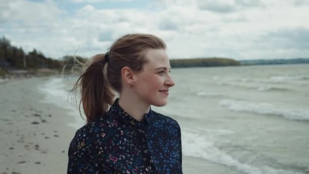 Femme blonde aux taches de rousseur marchant près de la plage tranquille par une journée venteuse — Video