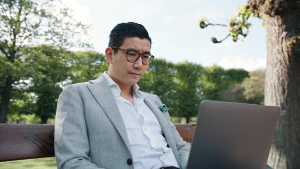 Homme d'affaires coréen sur ordinateur portable dans le parc de la ville — Video