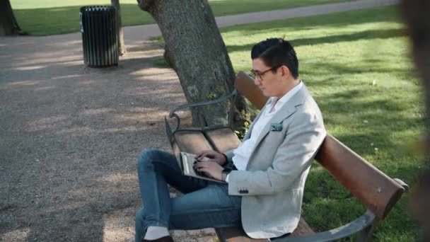 Empresario coreano en el parque de la ciudad usando el ordenador portátil — Vídeos de Stock