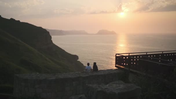 海の上で夕日を見るために座っているカップル — ストック動画
