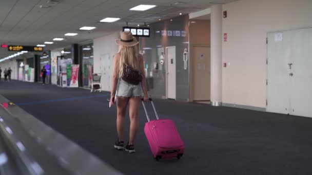 Back Walking da mulher no aeroporto com bagagem rosa na mão — Vídeo de Stock