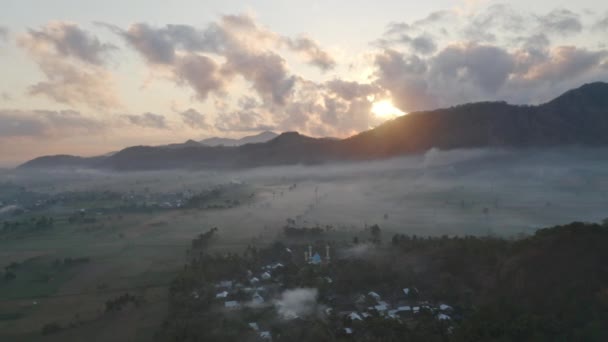 Campos lisos cercados por névoa branca e sol nascente atrás da montanha da floresta — Vídeo de Stock
