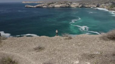 Uçurumun üstündeki adam Lombok 'a tepeden bakan bir uçakla İHA' yı kontrol ediyor.