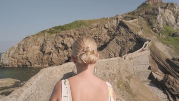 Alleinreisende geht auf Brücke in Gaztelugatxe in Spanien unter der Sonne — Stockvideo