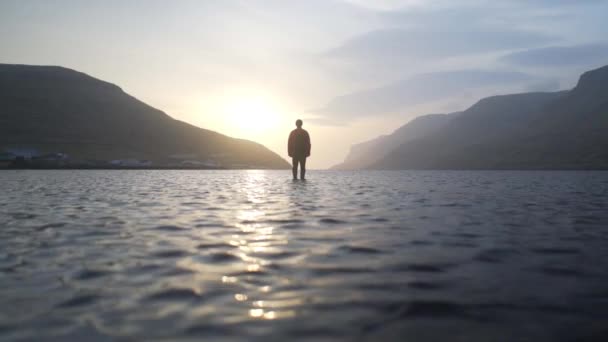 Homme debout au lever du soleil dans le lac peu profond — Video