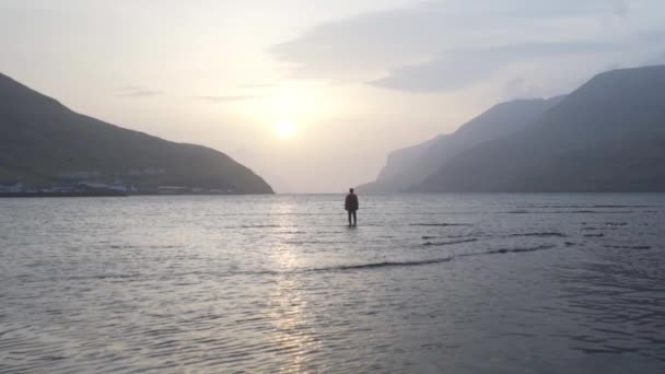 Людина стоїть у тихому озері на світанку — стокове відео