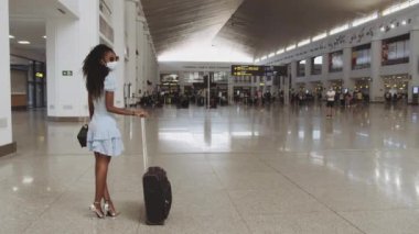 Havalimanında salgın sırasında maskeli güzel kıvırcık saçlı kadın.