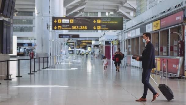 Homem com máscara cirúrgica pendurado baixo no queixo como ele passa através do aeroporto vazio — Vídeo de Stock