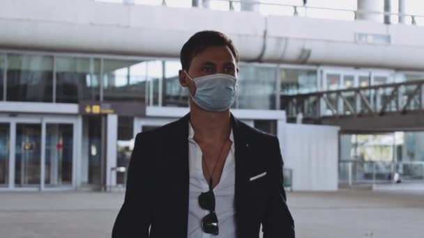 Людина в хірургічній масці і ділові костюми ходьба з зоною вильоту з аеропорту — стокове відео