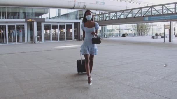 Mujer de moda en vestido azul caminando con máscara quirúrgica en la terminal del aeropuerto — Vídeo de stock