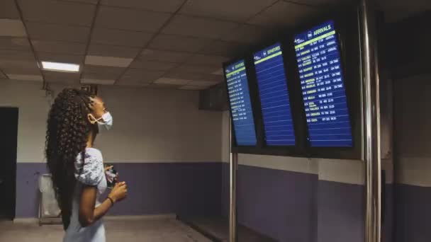 Schlanke Frau mit Maske kontrolliert Abflug- und Ankunftskontrolle am Flughafen — Stockvideo
