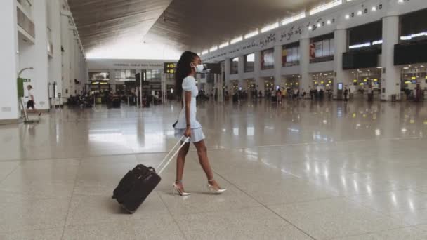 Mulher de cabelos encaracolados bonita na máscara durante a caminhada pandêmica no aeroporto — Vídeo de Stock