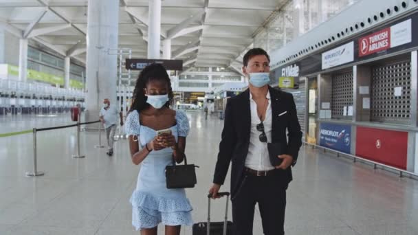 Homem e mulher com máscaras cirúrgicas no aeroporto com mulher ao telefone — Vídeo de Stock