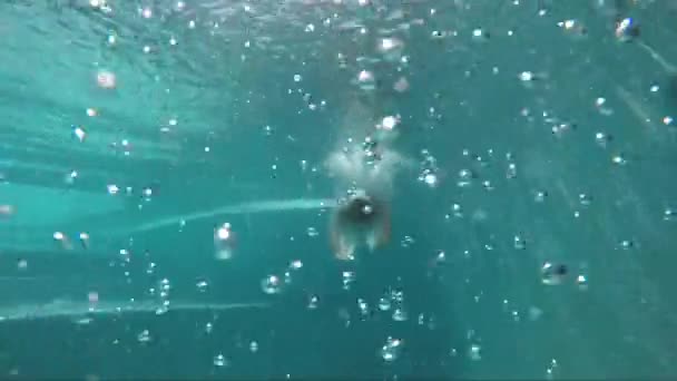 Bubbels op de voorgrond en de mens zwemmen onder water met zonnige stralen op de achtergrond — Stockvideo