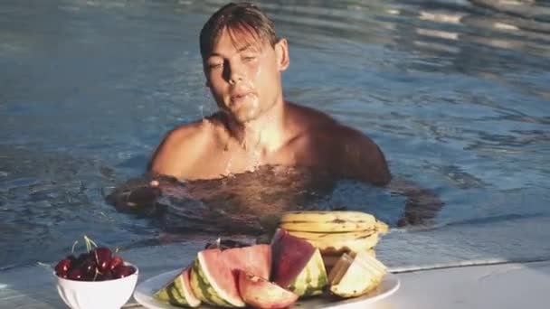 L'uomo che emerge dalla piscina per mangiare frutta — Video Stock