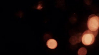 Sıcak, bulanık bir ateş ışığı, yumuşak, parıldayan bokeh küreleri çerçevenin üzerinde sürükleniyor, rüya gibi, atmosferik bir zemin oluşturuyor.