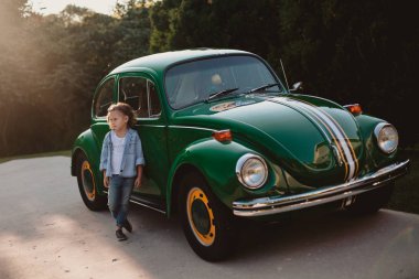 Eski moda arabanın yakınında oynarken gülümseyen küçük kız