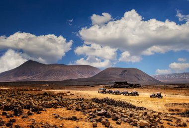 Birkaç at arabası sıraya girdi. Tepeleri olan harika bir çöl manzarası ve arkasında bulutlar olan güzel mavi bir gökyüzü. Fuerteventura, Kanarya Adası 'nda..