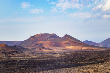 Kırmızı volkanik tepe kumlu çölde Timanfaya Milli Parkı'nda bir görüntü. Mavi bulutlar ile arka planda gökyüzüdür. Lanzarote, Kanarya Adaları, İspanya yer alır.