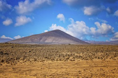 Volkanik tepe kumlu çölde bir görüntü. Mavi bulutlar ile arka planda gökyüzüdür. Fuerteventura, Kanarya Adaları, İspanya yer alır.