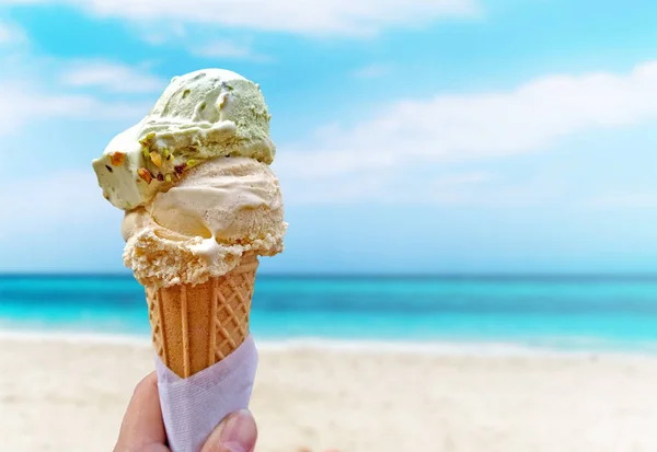 Hand is holding the vanilla ice cream. In the background is blue sky, sea nd sandy beach. This is situated in Varadero, Cuba.