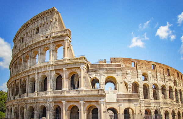 The Colosseum is in Roma, Italy. It is a large stone ruin. There is sunny day in summer. Blue sky is in the baground.
