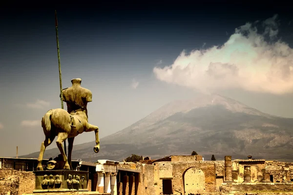 The stone statue of the roman hero in the middle of Pompei. Behind it is a view of the volcano Vesuvius. It is situated in historical area in Italy in Europe.