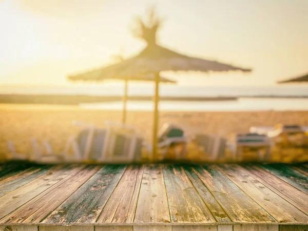 Wooden board empty table in front of blurred background. It can be used for display or montage your products. Sandy beach, umbrella palm leaves,crystal sea and the sun is in the summer background