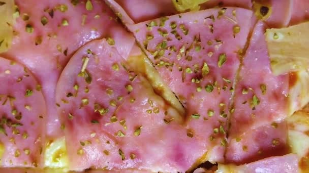 视频特写镜头的比萨饼夏威夷火腿 奶酪和菠萝 披萨上洒满了香料 罗勒和牛至 它是桌子上旋转比萨饼的下角视图 — 图库视频影像
