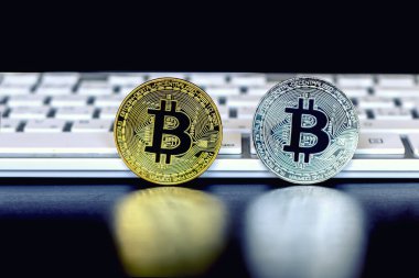 Bitcoin standları önünde beyaz klavye siyah zemin üzerine altın ve gümüş sikkeleri.