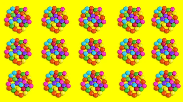 Colorful chocolade smarties on the yellow background with many chocolade bombones. It is circle shape.