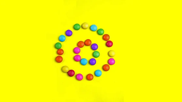Barevné čokoládky lentilky na žlutém podkladu. Je kruhového tvaru. — Stock fotografie