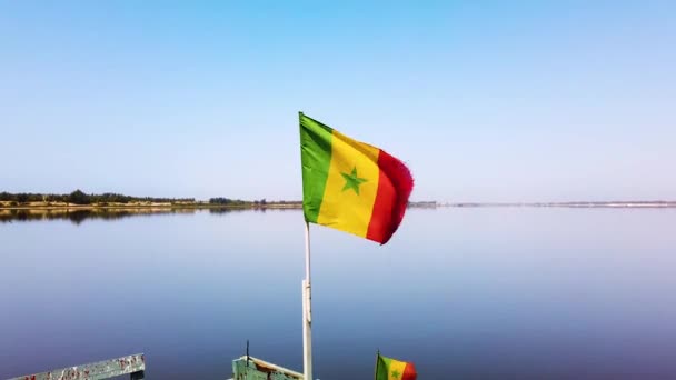 Vidéo 4K du drapeau sénégalais agitant sur le ciel bleu et le lac salé rose en arrière-plan, le Sénégal officiellement la République du Sénégal est un pays en Afrique de l'Ouest . — Video