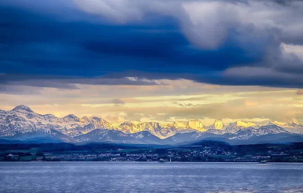 La ciudad de Constanza en el lago Constace, Bodensee. La vista de la puesta de sol en las montañas nevadas Alpes. Thelake se encuentra en Alemania, Austria y Suiza. — Foto de Stock